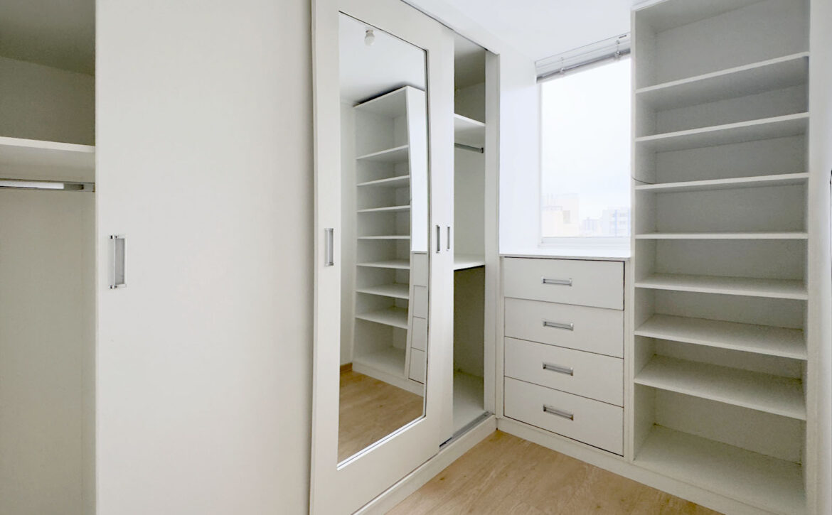 Walk-in closet del dormitorio principal con cajonera y espejo, departamento en venta en Lince