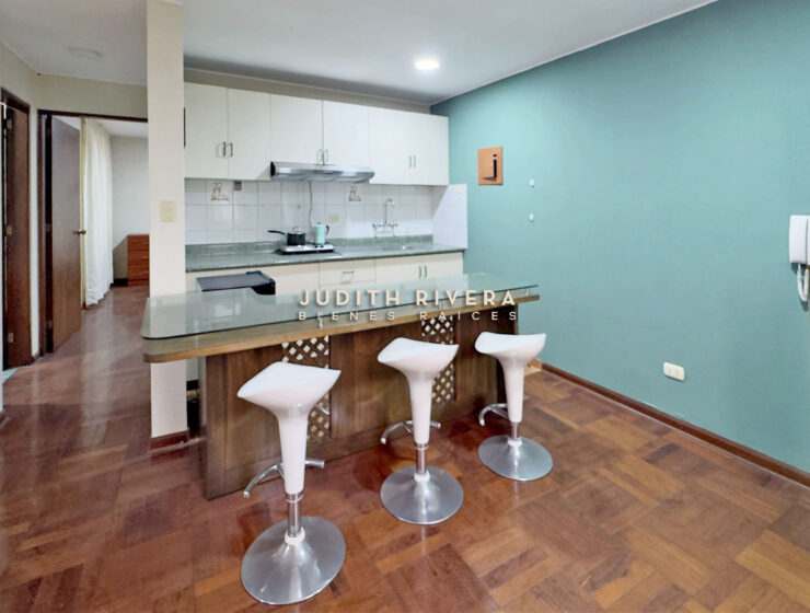 Cocina abierta del departamento en Santiago de Surco, con barra y tres taburetes blancos.