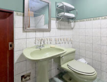 Baño completo con lavatorio, espejo y repisas sobre pared de azulejos blancos.