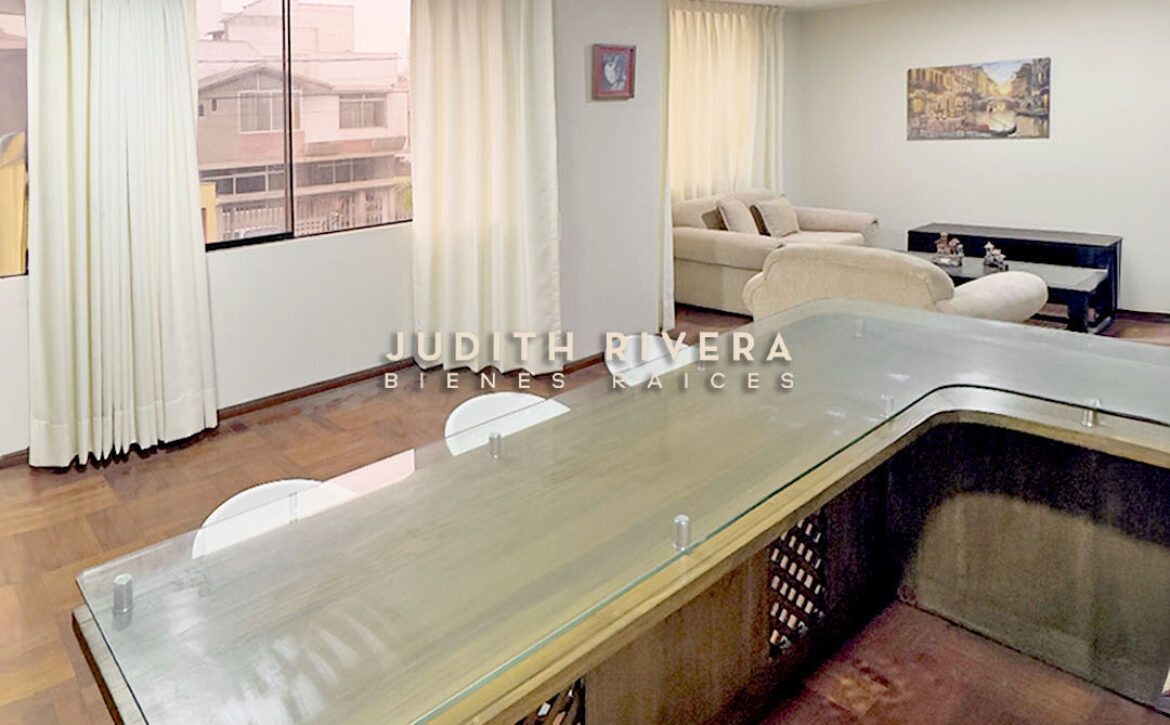 Sala comedor del departamento en Surco vista desde la barra de la cocina, con cortinas claras.