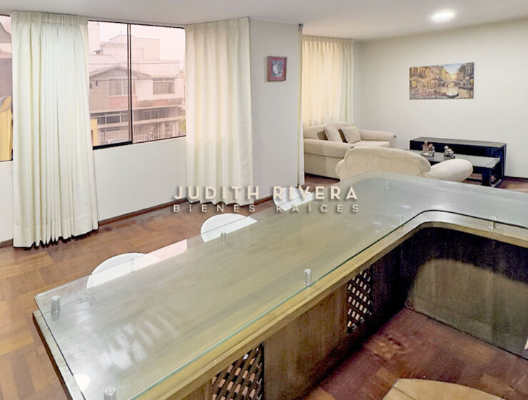 Sala comedor del departamento en Surco vista desde la barra de la cocina, con cortinas claras.