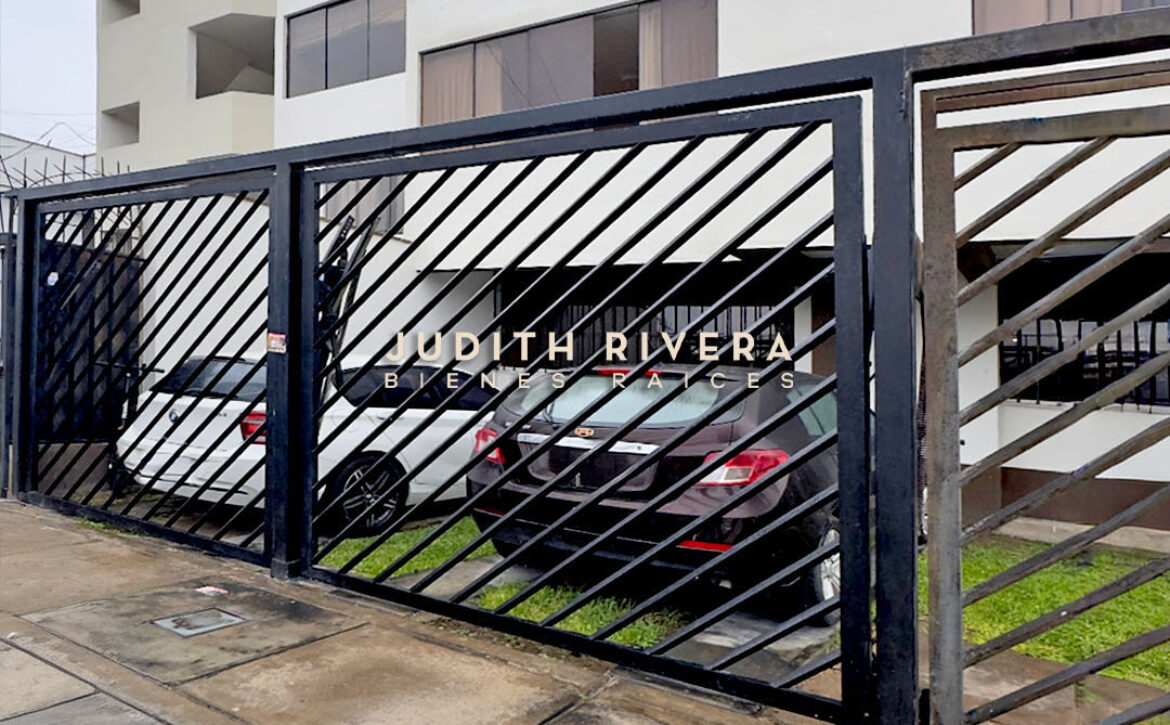 Cochera del edificio del departamento en alquiler en Santiago de Surco, con reja metálica.