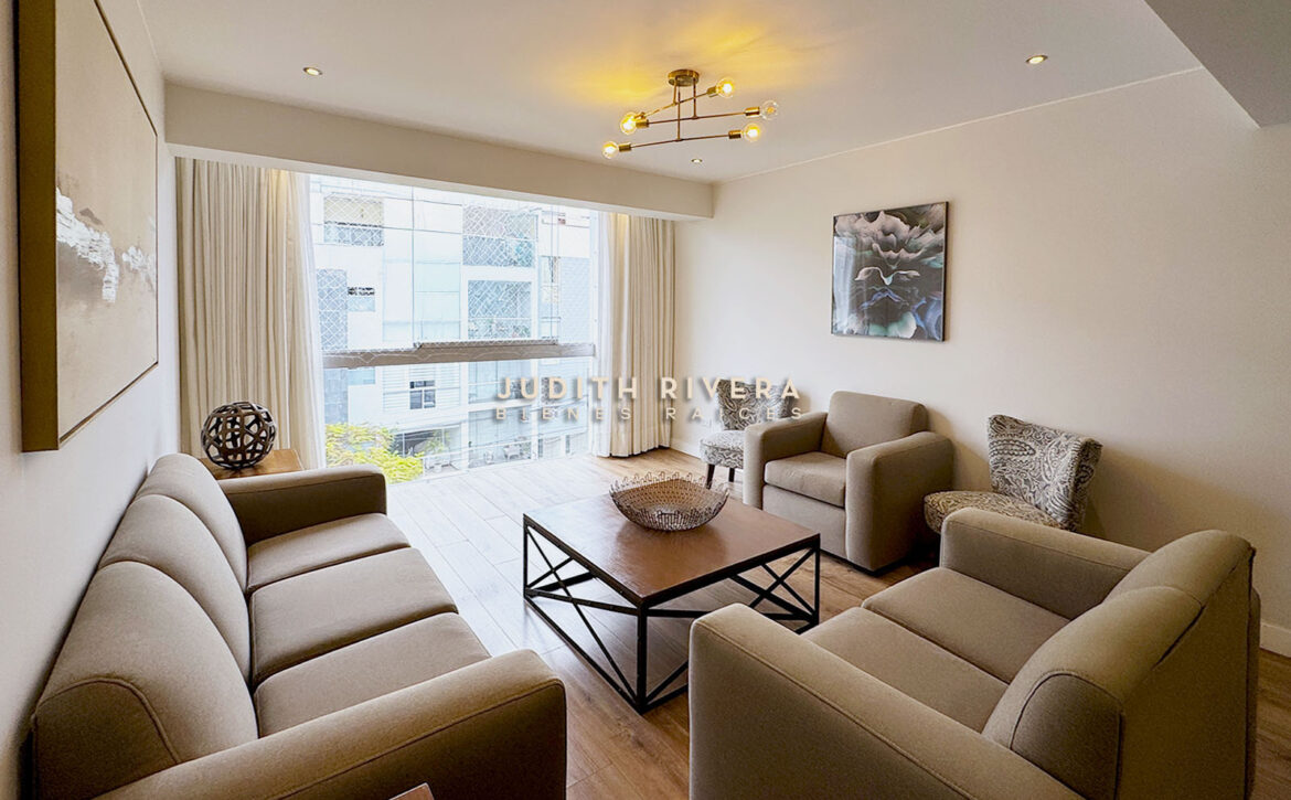 Departamento de 3 dormitorios en Surco: sala con ventanal de piso a techo, cortinas beige, sofás y mesa de centro de madera