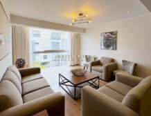 Departamento de 3 dormitorios en Surco: sala con ventanal de piso a techo, cortinas beige, sofás y mesa de centro de madera