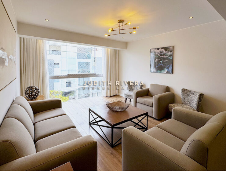 Departamento de 3 dormitorios en Surco: sala con ventanal de piso a techo, cortinas beige, sofás y mesa de centro de madera