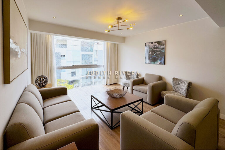 Departamento de 3 dormitorios en Surco: sala con ventanal de piso a techo, cortinas beige, sofás y mesa de centro de madera