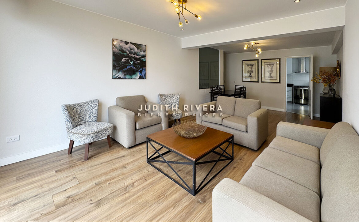 Sala comedor en un solo ambiente con piso de madera clara; al fondo, el comedor y la cocina