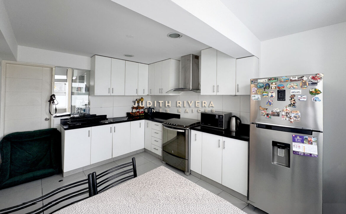 Cocina en L con refrigeradora de acero, campana y muebles blancos