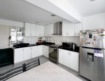Cocina en L con refrigeradora de acero, campana y muebles blancos