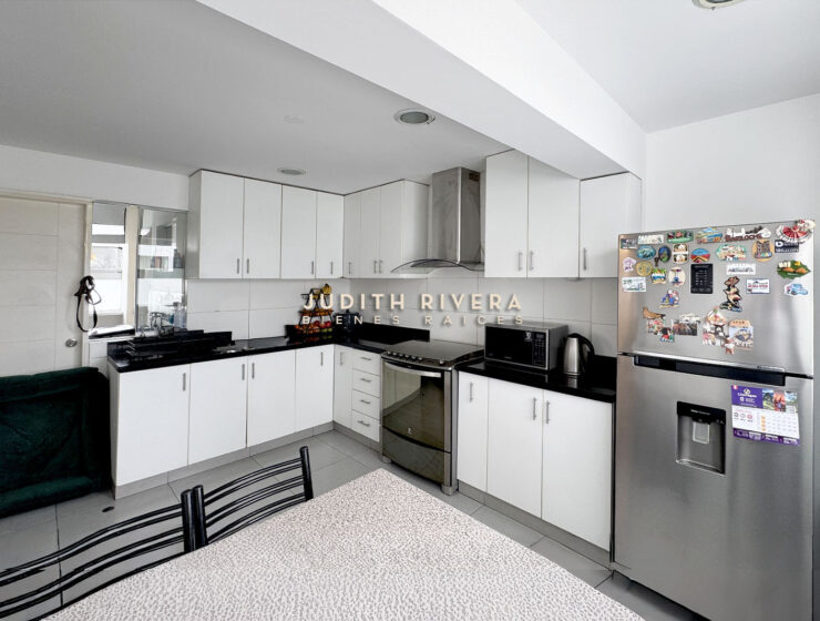 Cocina en L con refrigeradora de acero, campana y muebles blancos