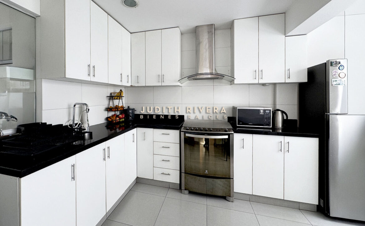 Cocina con muebles blancos, tablero negro, campana de acero y horno empotrado
