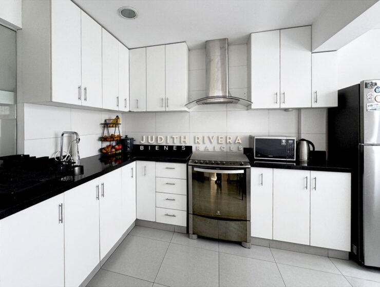 Cocina con muebles blancos, tablero negro, campana de acero y horno empotrado