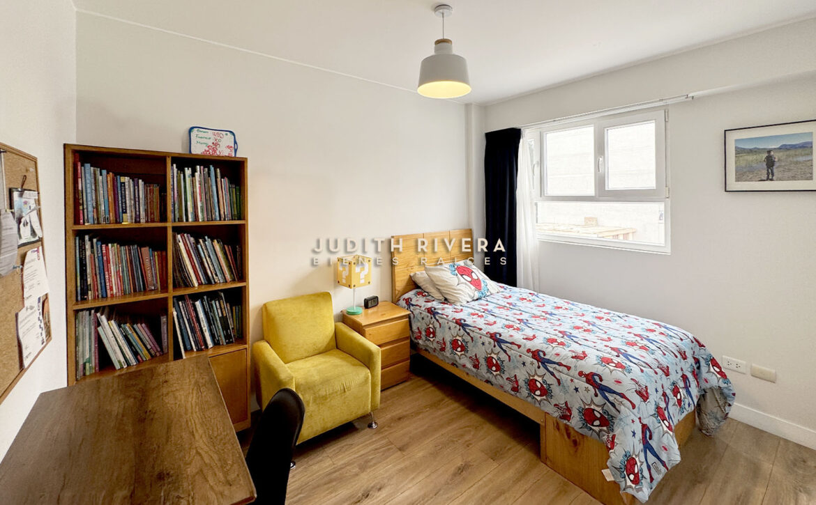 Dormitorio con librero, sillón amarillo, cama de plaza y media y ventana