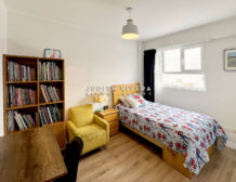 Dormitorio con librero, sillón amarillo, cama de plaza y media y ventana