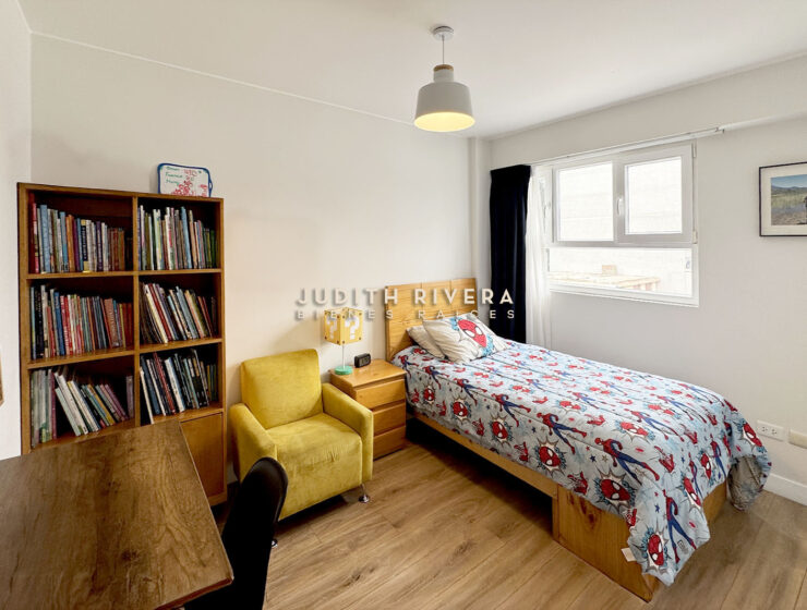 Dormitorio con librero, sillón amarillo, cama de plaza y media y ventana