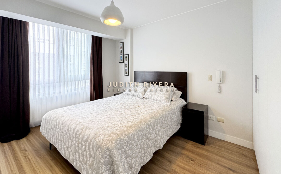 Dormitorio con cama de dos plazas, ventana amplia con cortinas oscuras y veladores