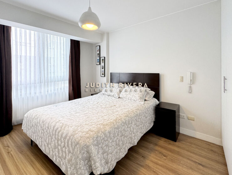 Dormitorio con cama de dos plazas, ventana amplia con cortinas oscuras y veladores