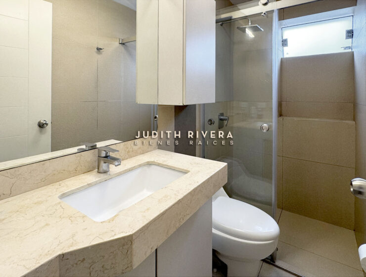 Baño con tablero de mármol claro, ducha con mampara de vidrio y ventana alta