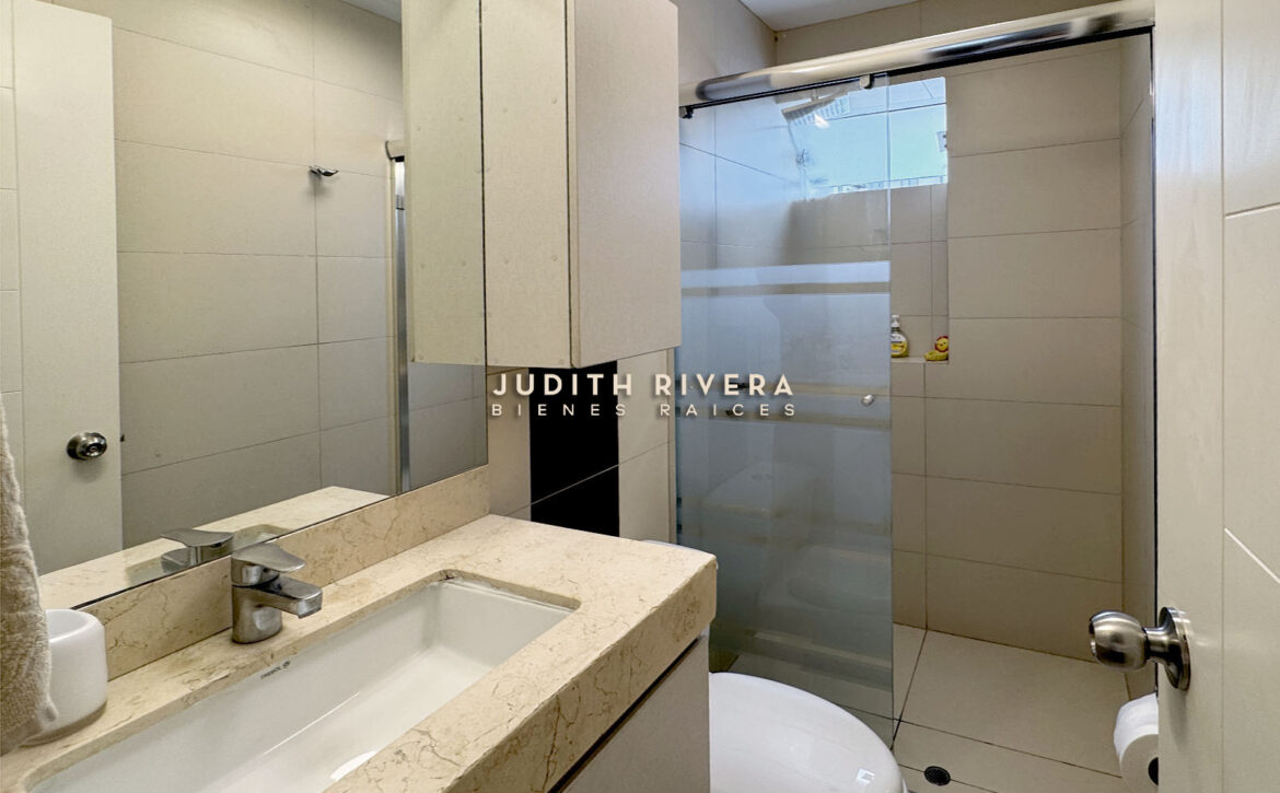 Segundo baño con ducha de mampara, tablero de mármol claro y mueble alto
