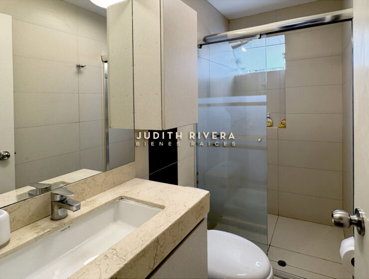 Segundo baño con ducha de mampara, tablero de mármol claro y mueble alto